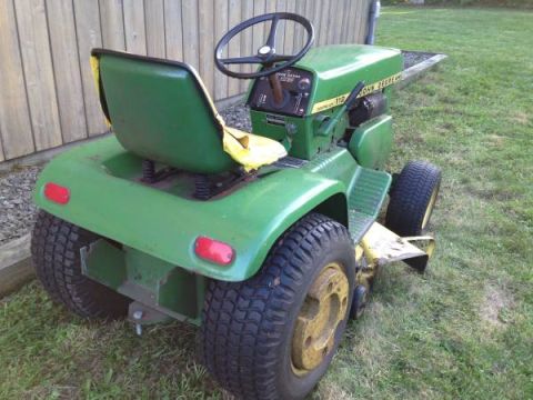 1982 Kubota RTV900 - A green John Deere lawn tractor with a yellow seat is parked on grass.