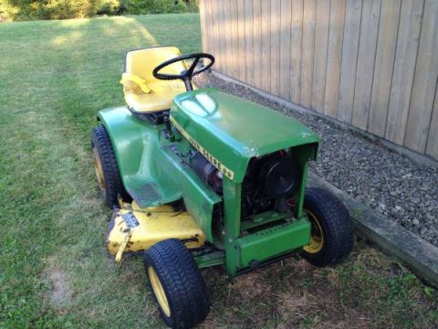 1982 Kubota RTV900 - A green and yellow John Deere riding lawn mower is parked on a grassy area next to a wooden fence.
