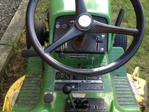 1982 Kubota RTV900 - The interior of a green John Deere lawn tractor, showing the steering wheel, gear shifter, and various warning labels.