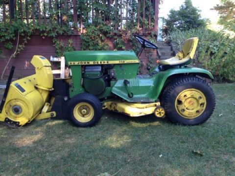 1982 Kubota RTV900 - John Deere 112 lawn tractor equipped with a snow blower attachment sits on a grassy lawn.