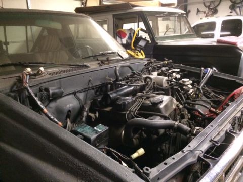1988 Suzuki Samurai - The engine compartment of a vehicle is open, revealing the engine and associated components. Another vehicle is parked behind it.