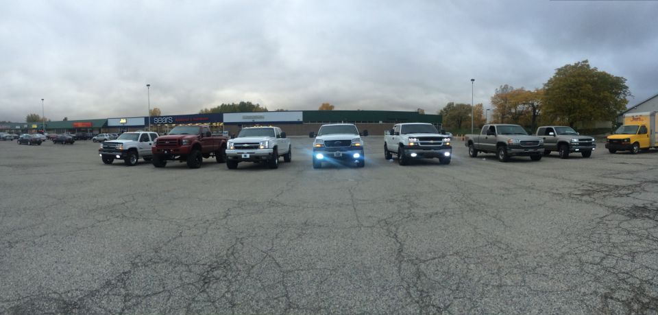 Several Chevrolet Silverado trucks parked in a lot, one with bright headlights