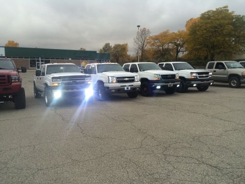 2006 Chevrolet Silverado 2500 - A line of white pickup trucks are parked in a lot under an overcast sky.