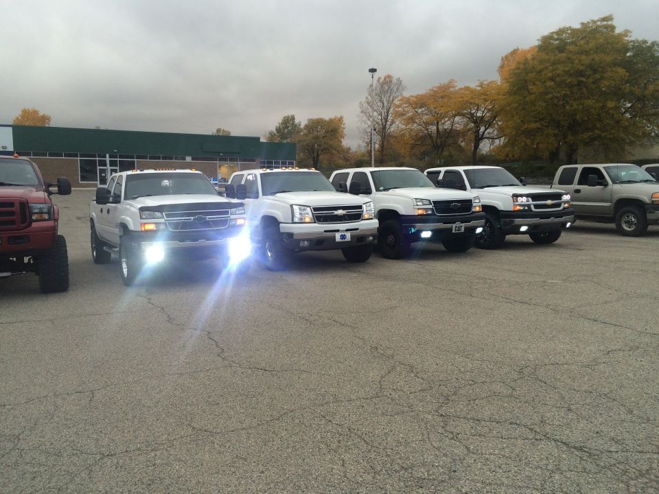 Several white pickup trucks parked in a lot, one red truck on the left