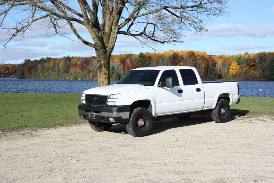 White 2006 Chevrolet Silverado 2500 parked by a lake with fall foliage