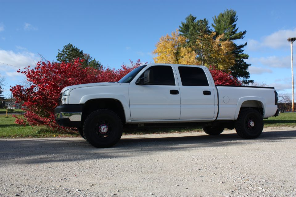 White 2006 Chevrolet Silverado 2500 pickup truck parked on a gravel road with red and yellow trees in the background