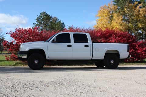 2006 Chevrolet Silverado 2500 - A white 2006 Chevrolet Silverado 2500 pickup truck is seen from the side, parked outdoors with autumn foliage in the background.