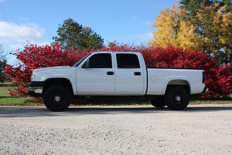 White 2006 Chevrolet Silverado 2500 pickup truck parked on a gravel road with red and yellow trees behind it