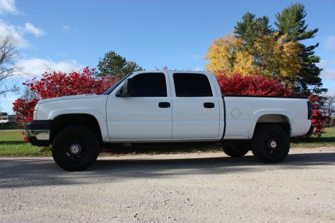 2006 Chevrolet Silverado 2500 - A white pickup truck is parked on a gravel road with colorful autumn foliage in the background.