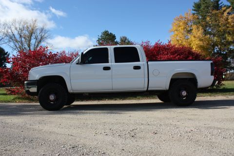 2006 Chevrolet Silverado 2500 - A white 2006 Chevrolet Silverado 2500 crew cab pickup truck is parked on a gravel road with fall foliage in the background.