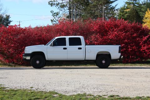 2006 Chevrolet Silverado 2500 - A white pickup truck is parked on a gravel road with a backdrop of vibrant red foliage.