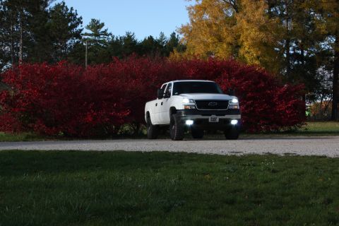 2006 Chevrolet Silverado 2500 - A white 2006 Chevrolet Silverado 2500 is parked on a gravel road with red and yellow foliage in the background.