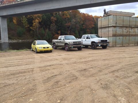 2006 Chevrolet Silverado 2500 - Two Chevrolet Silverado trucks and a yellow Volkswagen Jetta are parked outdoors under a bridge.