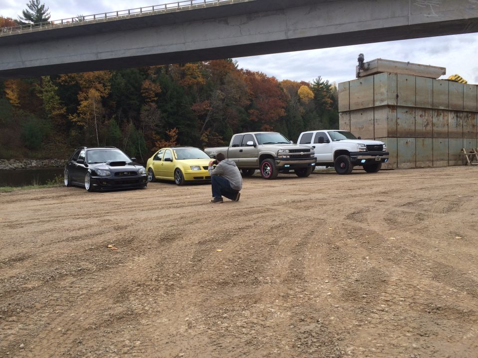 Silver Subaru WRX, yellow Volkswagen Jetta, silver Chevrolet Silverado 2500, and white Chevrolet Silverado 2500 parked under a bridge