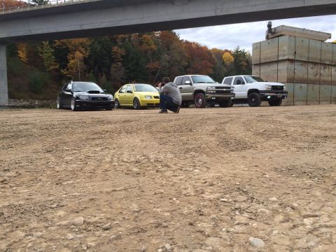 2006 Chevrolet Silverado 2500 - A photographer kneels to capture a lineup of four vehicles parked under a bridge.