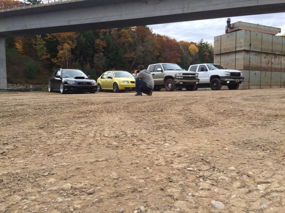 guy taking photo of four vehicles: black Subaru, yellow VW, silver truck, white truck