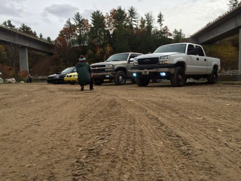 2006 Chevrolet Silverado 2500 - A white 2006 Chevrolet Silverado 2500 is parked in a lot with other vehicles, a person is crouching in front of it.
