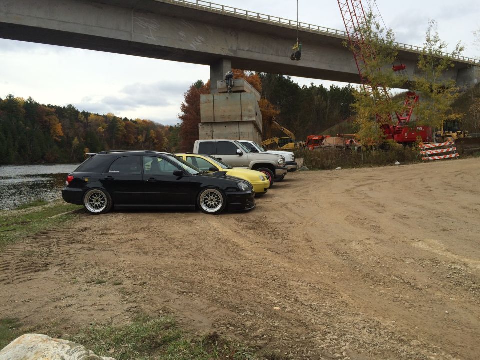Silver pickup truck parked on dirt lot under a bridge