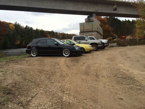 2006 Chevrolet Silverado 2500 - A lineup of vehicles, including a black station wagon, yellow sedan, and two pickup trucks, are parked on a dirt lot near a body of water a…