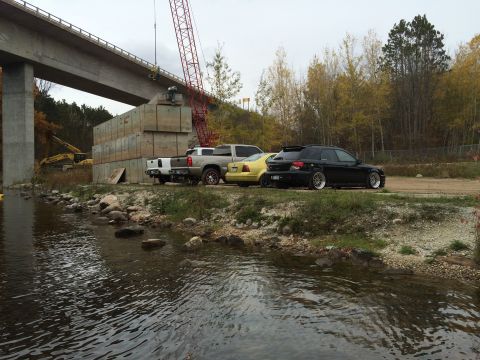 2006 Chevrolet Silverado 2500 - Several vehicles are parked near a river next to a construction site with a bridge and crane.