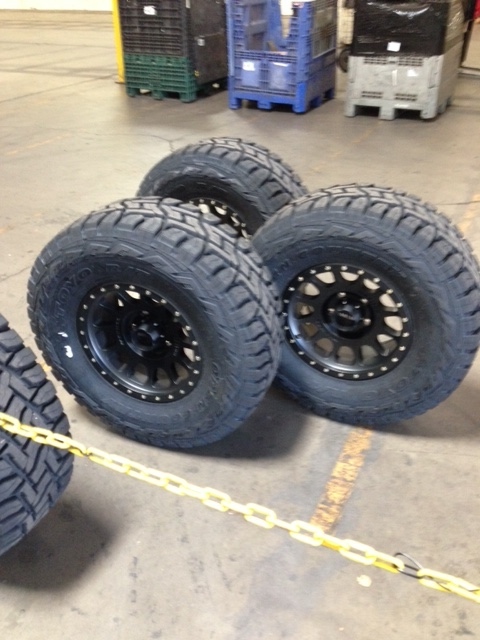 1996 Ford Bronco - Four off-road tires and rims are arranged on a concrete floor with yellow chain in the foreground.