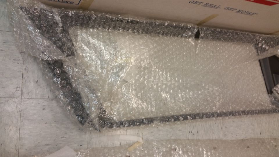 Partially unwrapped rectangular object with dark frame and white interior, covered in bubble wrap