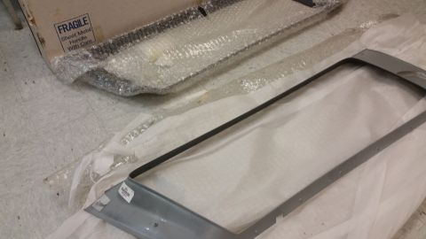 1987 Dodge 1500 - Unidentified gray metal part with black trim, packaged for shipping. Text on box reads 'FRAGILE Sheet Metal Handle With Care'.