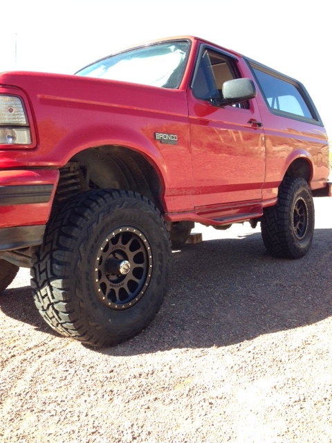 1996 Ford Bronco - This red Ford Bronco is shown from the front quarter angle, highlighting its lifted suspension and off-road tires.