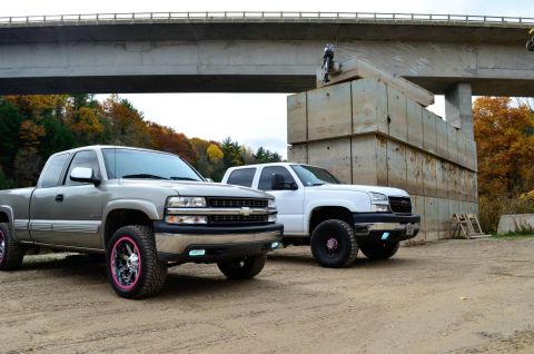 2006 Chevrolet Silverado 2500 - Two Chevrolet Silverado 2500 trucks are parked outdoors under a bridge, with one having custom pink rims.