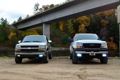 2006 Chevrolet Silverado 2500 - Two Chevrolet Silverado 2500 trucks are parked side-by-side under a concrete bridge with autumn foliage in the background.
