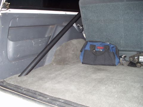 1993 Ford Bronco - The rear interior of a vehicle shows a roll cage, a tool bag, and a jack on the carpeted floor.