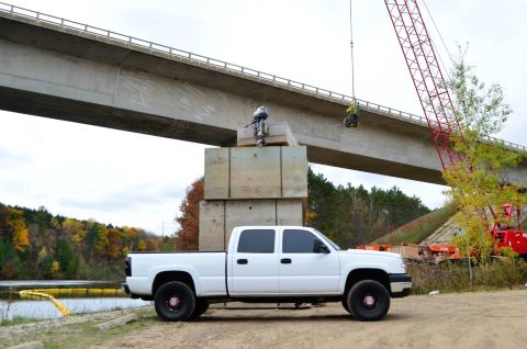 2006 Chevrolet Silverado 2500 - A white 2006 Chevrolet Silverado 2500 pickup truck is parked near a body of water, with a bridge and construction equipment in the backgrou…