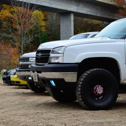 2006 Chevrolet Silverado 2500 - Multiple pickup trucks are lined up on a dirt road with a bridge and fall foliage visible.