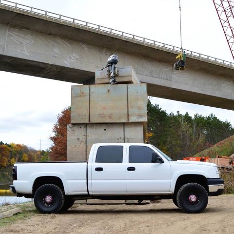 2006 Chevrolet Silverado 2500 - A white 2006 Chevrolet Silverado 2500 is parked under a bridge, with a boat motor suspended above it.