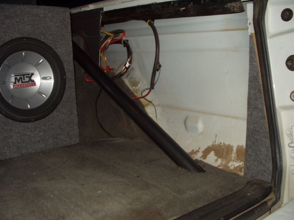 MTX subwoofer box beside exposed white sheet metal and wiring in vehicle cargo area