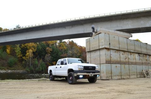 2006 Chevrolet Silverado 2500 - White pickup truck parked near a large concrete structure and a bridge.