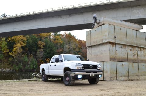 2006 Chevrolet Silverado 2500 - A white pickup truck is parked on a dirt lot under a bridge, with a body of water and trees in the background.