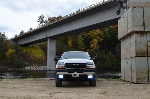 2006 Chevrolet Silverado 2500 - A white 2006 Chevrolet Silverado 2500 is parked by a river with a bridge overhead and concrete blocks to the side.