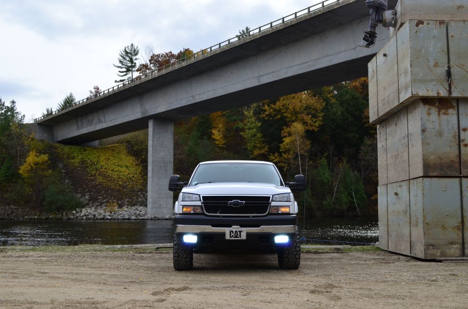 Front view of a white 2006 Chevrolet Silverado 2500 parked near a river under a bridge. It has a CAT emblem on the front
