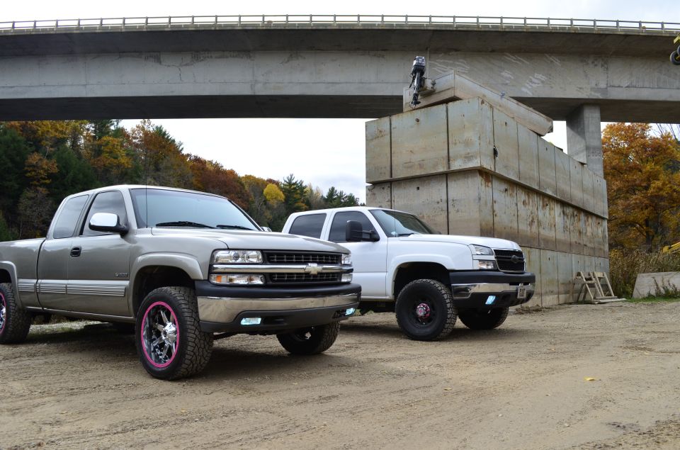 Silver pickup with pink rims and white pickup parked under a bridge