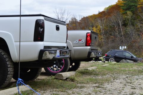 2006 Chevrolet Silverado 2500 - Two pickup trucks and a dark SUV are parked outdoors with autumn foliage in the background.