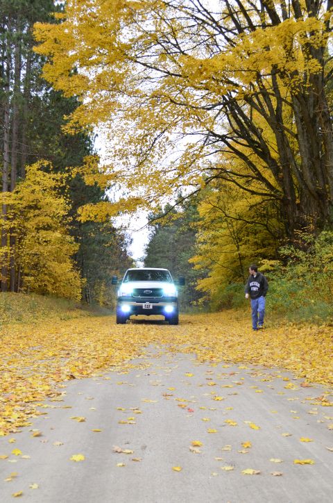 2006 Chevrolet Silverado 2500 - A white 2006 Chevrolet Silverado 2500 drives down a road lined with trees in autumn.