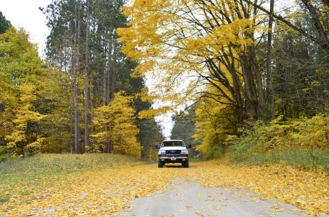 2006 Chevrolet Silverado 2500 - A white 2006 Chevrolet Silverado 2500 drives through a scenic autumn landscape with trees shedding yellow leaves.