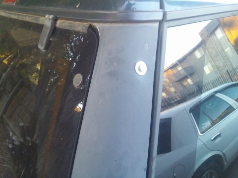 2000 Mercury Grand Marquis - A close-up view of the rear pillar and trim of a vehicle, with another car reflected in the window.