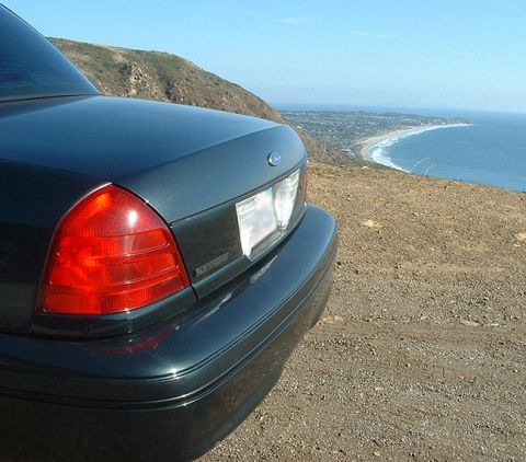 1998 Ford Crown Victoria - Rear taillight, trunk, and Ford emblem of a dark green sedan parked at a coastal hilltop overlook.