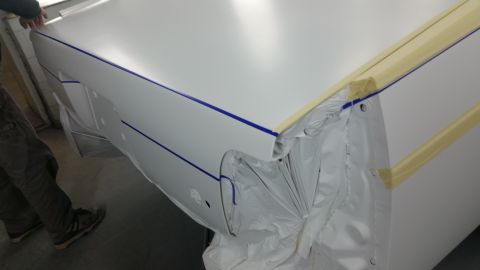 1991 Ford LTD Crown Victoria - A person is preparing a car's body panels for a fresh coat of paint, with masking tape and plastic sheeting in place.