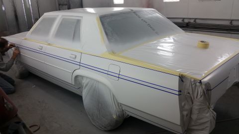1991 Ford LTD Crown Victoria - A person applies blue pinstripes to a white sedan that is covered in protective plastic sheeting.