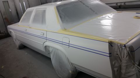 1991 Ford LTD Crown Victoria - A white sedan is covered in protective plastic and tape, likely in a paint booth, awaiting a new coat of paint.