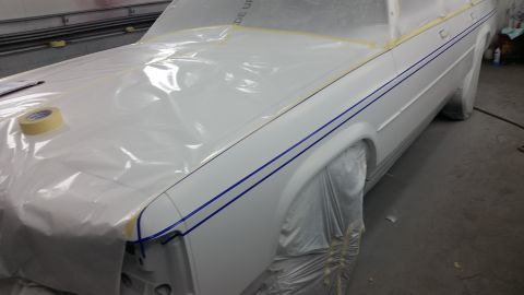 1991 Ford LTD Crown Victoria - A white car with blue pinstripes is covered in plastic and tape, likely in a body shop for preparation before painting.
