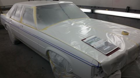 1991 Ford LTD Crown Victoria - Car covered in plastic sheeting in a paint booth, binder of photos on the hood.